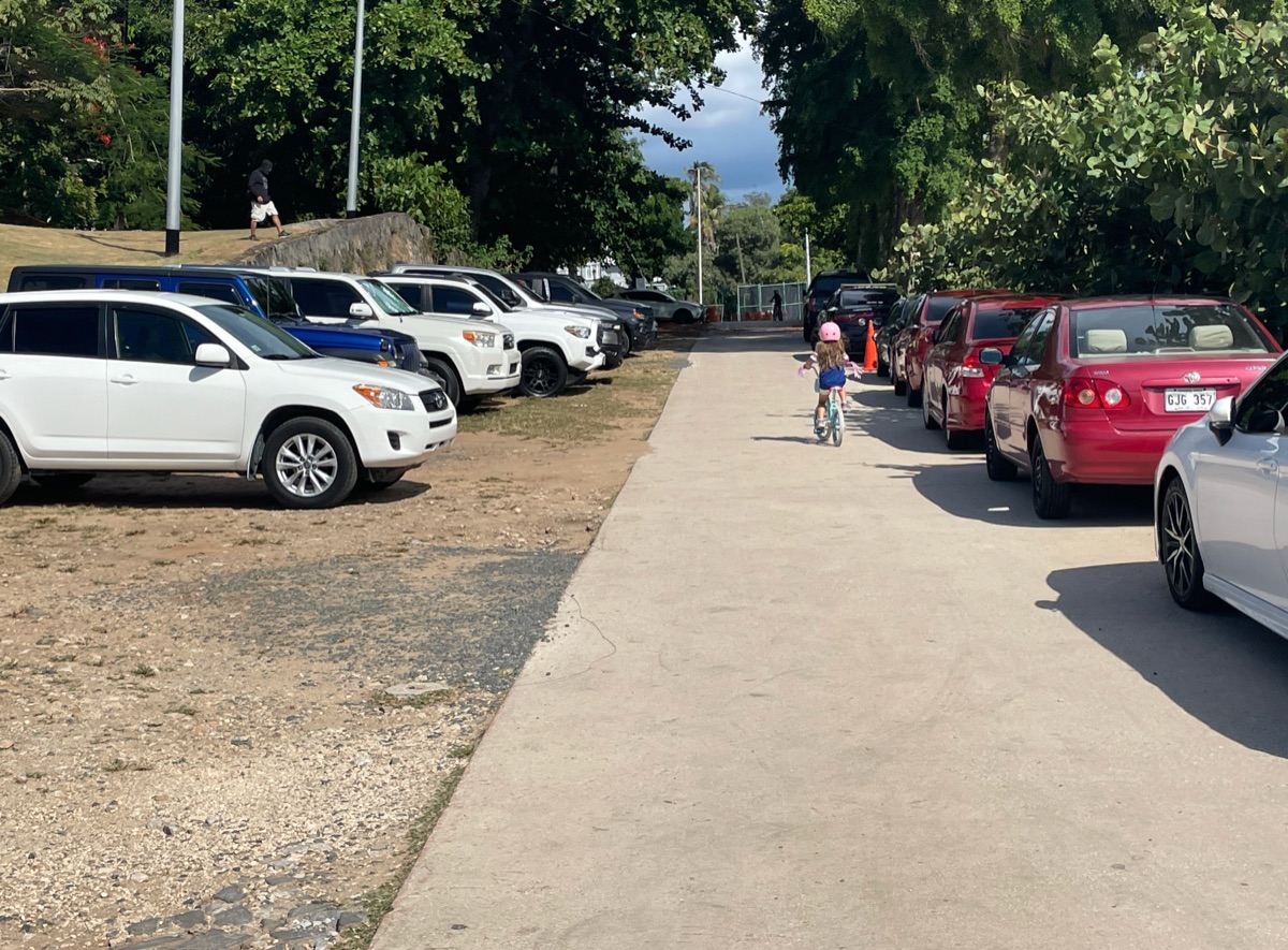 Niña en bicicleta circulando entre carros estacionados